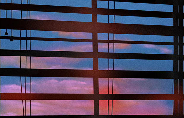 The sun sets behind a set of blinds